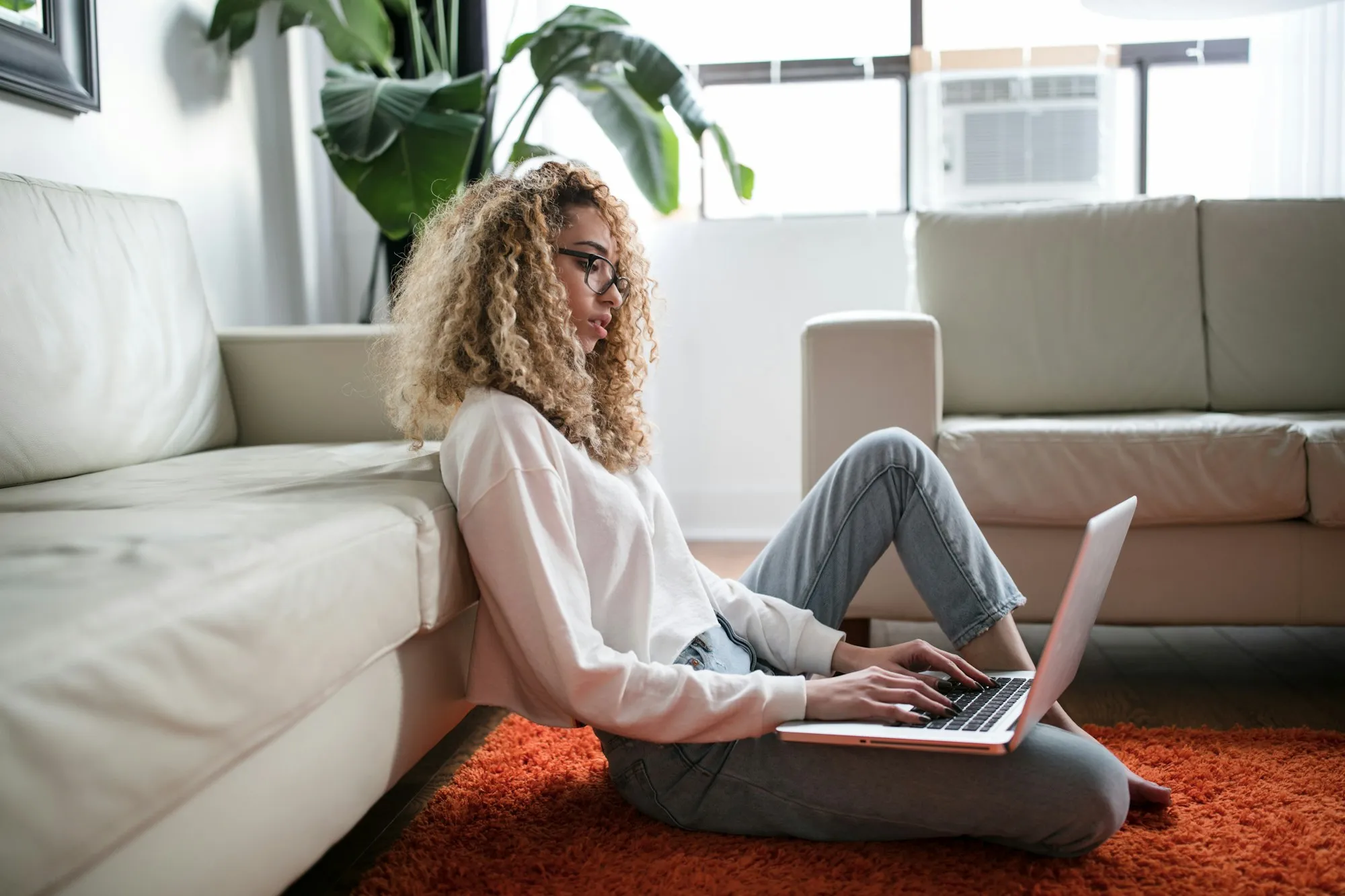 A young woman working on a laptop while sitting on a living room floor
